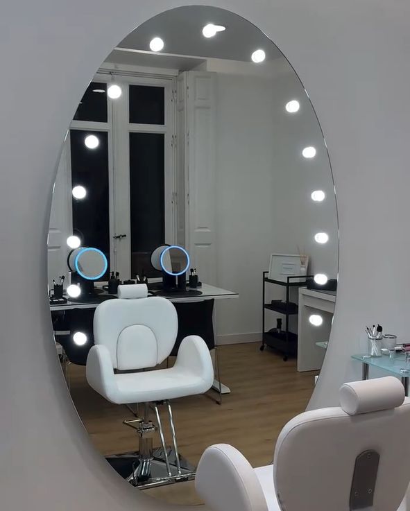 Espejo ovalado con bombillas junto a un sillón blanco en el estudio de Sumakeup